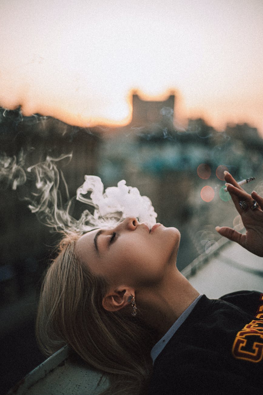 woman lying on a roof of a building and smoking a cigarette