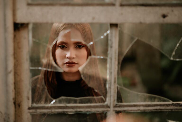 calm young woman looking at camera through broken window