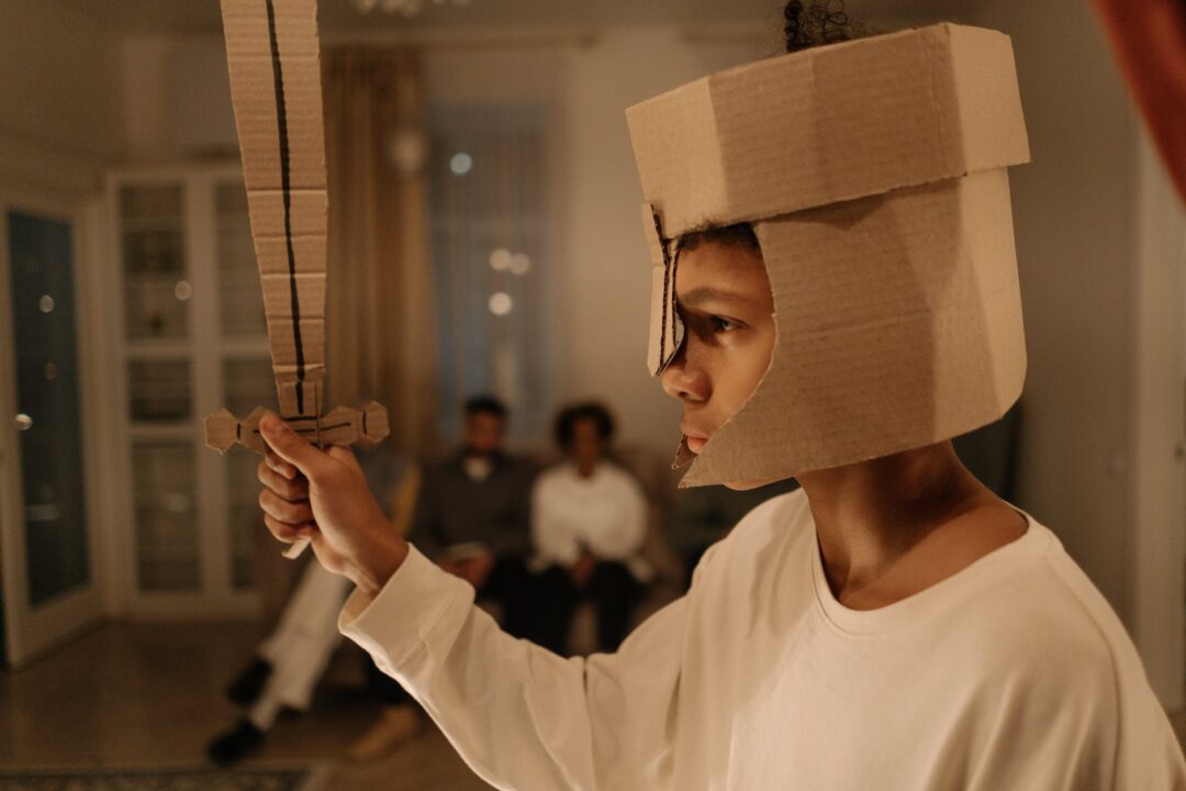 boy in white long sleeve shirt holding brown cardboard sword