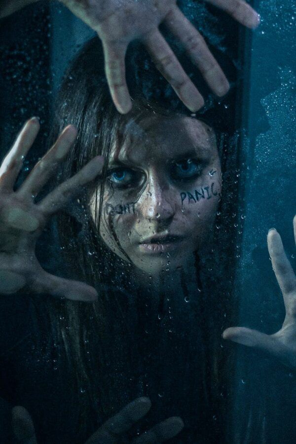 girl with wet hair and smudged makeup holding her hands on a wet window
