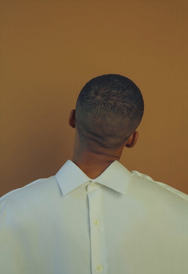black man in white shirt standing behind wall